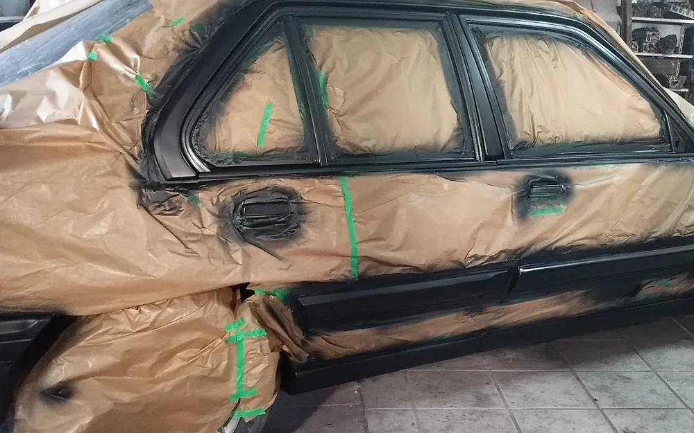 Carro mascarado com papel e fita na oficina, com a lateral já pintada de preto