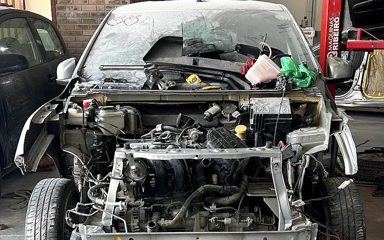 Frente de um carro desmontada para reparo de colisão, com a estrutura e o motor à mostra
